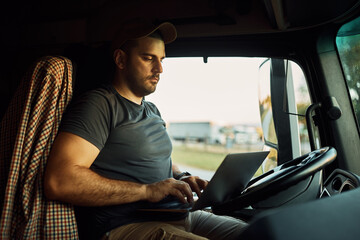 Truck driver working on laptop while sitting in cabin.