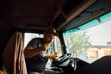 Young truck driver eating lunch inside of his vehicle.