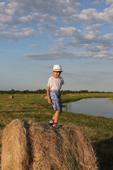 Naklejka na ściany i meble Russian tourist child, fashion kid, cute boy in village in Russia. Summer nature, landscape. Outdoor recreation, fun rest. Child with white hat. Look, outfit of child, kid. Summer vacation, travel