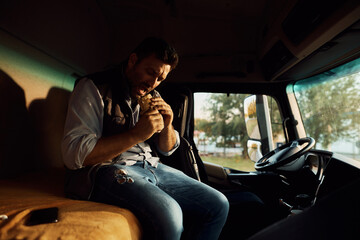 Truck driver eating sandwich while having lunch break on parking lot.