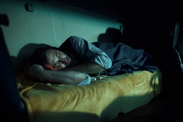 Tired truck driver sleeping on cabin's bed at night.