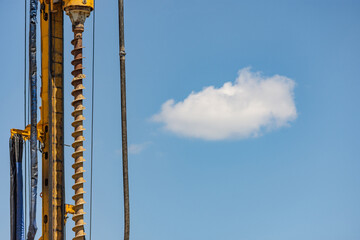 Yellow vertical drilling machine against blue sky with a cloud behind