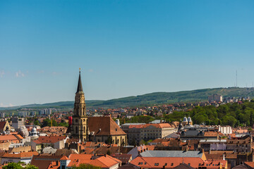 Cityscape of Cluj Napoca with church and vintage buildings on clear blue sky. Aerial view of an old town with hills in the distance