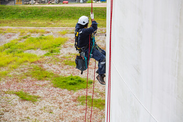 Obraz premium Top view male worker inspection wearing safety first harness rope safety line working at a high place on tank roof spherical