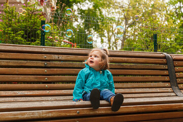 portrait of a little girl in the park on a bench catches soap bubbles