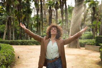 Mature and attractive woman, independent, successful, empowered with brown leather jacket and jeans with open arms giving thanks to life very happy. Concept happiness, triumph, empowerment.