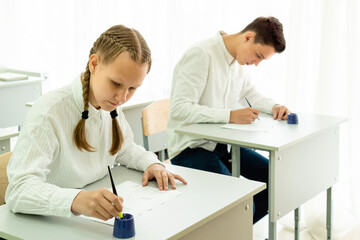 Two young students, an attractive dark-haired man and a blonde woman, are working on a project in the classroom, sitting at the table of a light class. High quality photo