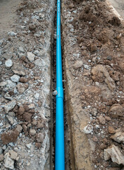 The new PVC pipe is laying in the trench near the asphalt road.