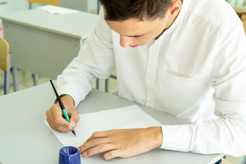 A student writes with a fountain pen while studying at school, sitting at a desk. Portrait of a college guy writing with a pen while completing a task. High quality photo