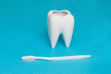 Fototapeta na wymiar The concept of dental health and dental care. Dentist's day. A white toothbrush lies next to a white tooth on a blue background. A healthy tooth. Space for text. Close-up