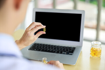 close up and silective focus rear viev doctor hands holding Omega-3 pills  and laptop computor on the table in office , healthy food supplements concept,