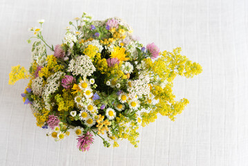 Summer blooming delicate flowers in a round vase on a table with a white tablecloth, a pastel...