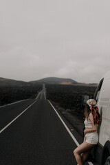 joven chica posando sobre su furgoneta con un bonito paisaje volcánico en Lanzarote y una carretera recta