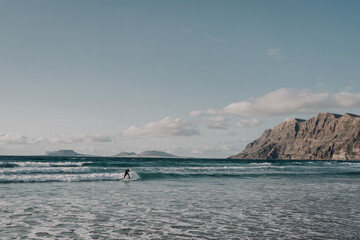 joven haciendo surf en una preciosa playa con acantilados al fondo