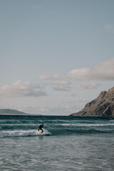 Obraz premium joven haciendo surf en una preciosa playa con acantilados al fondo