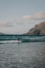 joven haciendo surf en una preciosa playa con acantilados al fondo