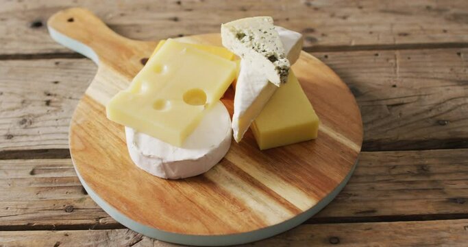 Video of assorted hard and soft cheeses on wooden chopping board and rustic table, with copy space