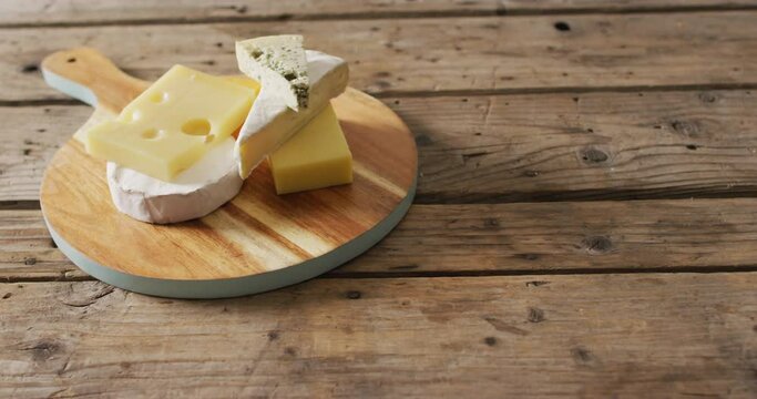 Video of assorted hard and soft cheeses on wooden chopping board and rustic table, with copy space