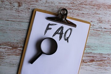 Top view image of paper clipboard with text FAQ or frequently asked question and magnifying glass.