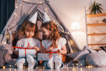 Holiday surprise. With gift boxes. Two little girls is in the tent in domestic room together
