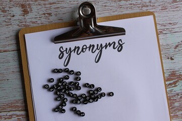 Top view image of paper clipboard with text synonyms and alphabet beads.