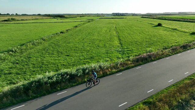 Man cycling on a winding country road during sunset seen from above. The drone is following the cyclist.