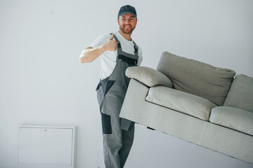 Lifting the sofa. Repairman is working indoors in the modern room