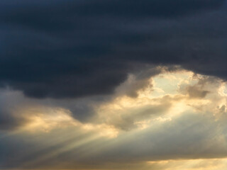 Skyscape with sunlight bursting through the leaden gloom of heavy storm clouds.