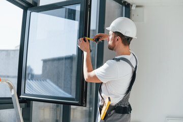 Using measure tape. Repairman is working indoors in the modern room