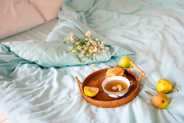 Obraz na płótnie Canvas a cup of hot tea with chamomile on a tray in bed. Blue sheets with breakfast in bed.