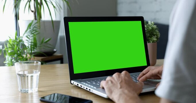 man sitting at desk and using laptop computer at home. scrolling the website. mockup with blank green screen