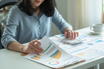 Portrait of a female accountant using a calculator and laptop to calculate balance using graphs for customers.