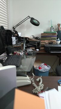 Dolly across messy desk in cluttered office with piles of files and coffee cup.  Vertical Video