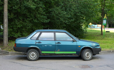 An old rusty broken Soviet car is parked near the lawn, Oktyabrskaya Embankment, St. Petersburg, Russia, August 2022