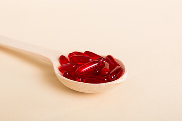 Vitamin capsules in a spoon on a colored background. Pills served as a healthy meal. Red soft gel vitamin supplement capsules on spoon