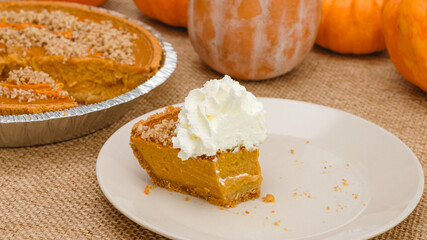 Slice of fresh baked homemade pumpkin pie decorated with crushed nuts and orange zest close up on a plate with whipped cream