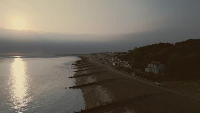 Garbage Trash Truck Lorry driving along beach front at sunrise Whitstable Beach with beach huts 