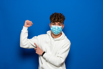 Portrait of a handsome man in a medical protective mask standing with his arms raised shows strong biceps. isolated background. Concept of staying strong and healthy against coronavirus covid-19.
