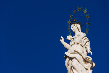 Fototapeta na wymiar Statue of Virgin Mary of the Stars at the top of an ancient column in the historic center of Lucca, erected in 1687 (with blue sky and copy space)