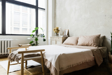 Bohemian styled cozy bedrom with king sized bed and big windows, grey antique furniture by left side of with greenery and and a Greek statue. Bench at the bottom of the bed