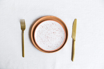 Set of clay plates of orange color, knife and fork on a white tablecloth of their natural material. Top view.