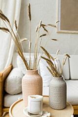 Living room decor. Dry wheat stands in ceramic vases on a wooden table next to a cozy light sofa