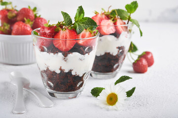 Trifles. Brownies, fresh strawberry and mascarpone cream servered in layers on glass on white background. Portion desserts. No baked brownie cheesecake with fresh berries in a glass.