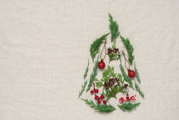 Christmas tree made of coniferous branches and decorations flat lay on a beige textile background....