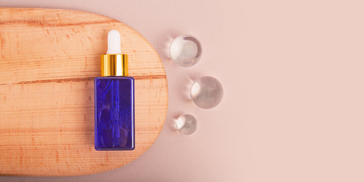Top view of cosmetics dropper on wooden slice with flass balls near it.Earth tones,good as cosmetic mockup,banner with copy space.