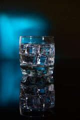 A glass with ice water and ice cubes on a blurred blue background. A refreshing and chilling drink in hot weather.