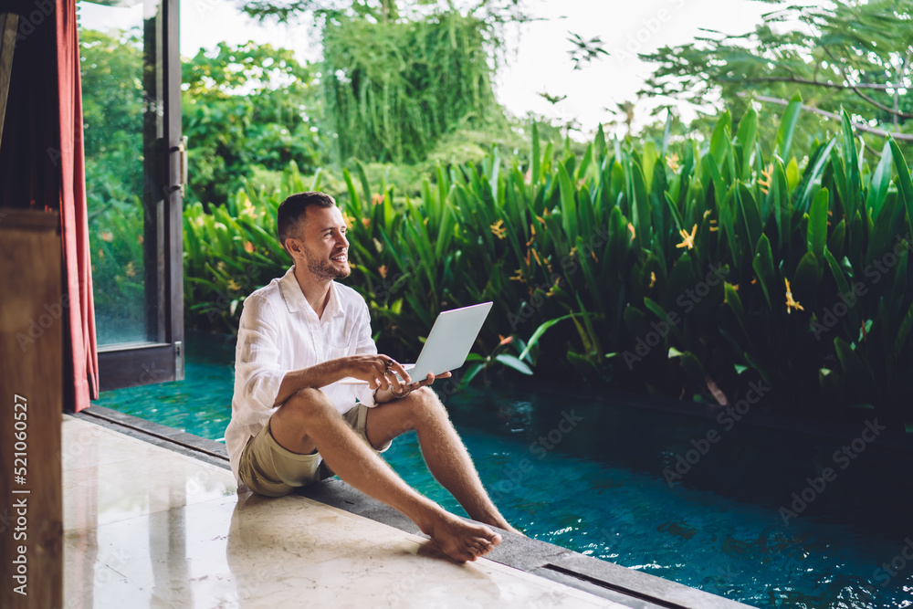 Wall mural Successful copywriter with modern laptop device enjoying time at pool terrace during summer vacations at Bali, happy male digital nomad with netbook computer smiling outdoors - freelance lifestyle