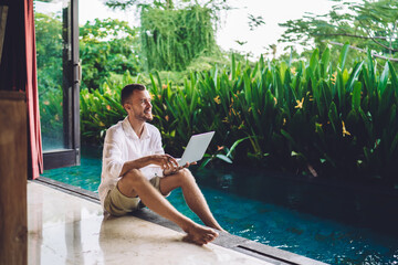 Successful copywriter with modern laptop device enjoying time at pool terrace during summer...