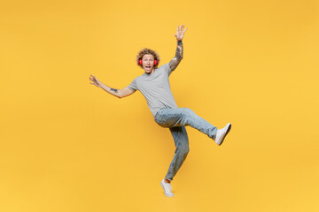 Fototapeta na wymiar Full body young man 20s he wear grey t-shirt headphones listen to music stand on toes with outstretched hands raise up leg isolated on plain yellow backround studio portrait. People lifestyle concept.