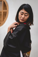 Portrait of sexy and young japanese girl with beautiful old traditional red kimono and black yukata in front of a old white wall in a japanese garden